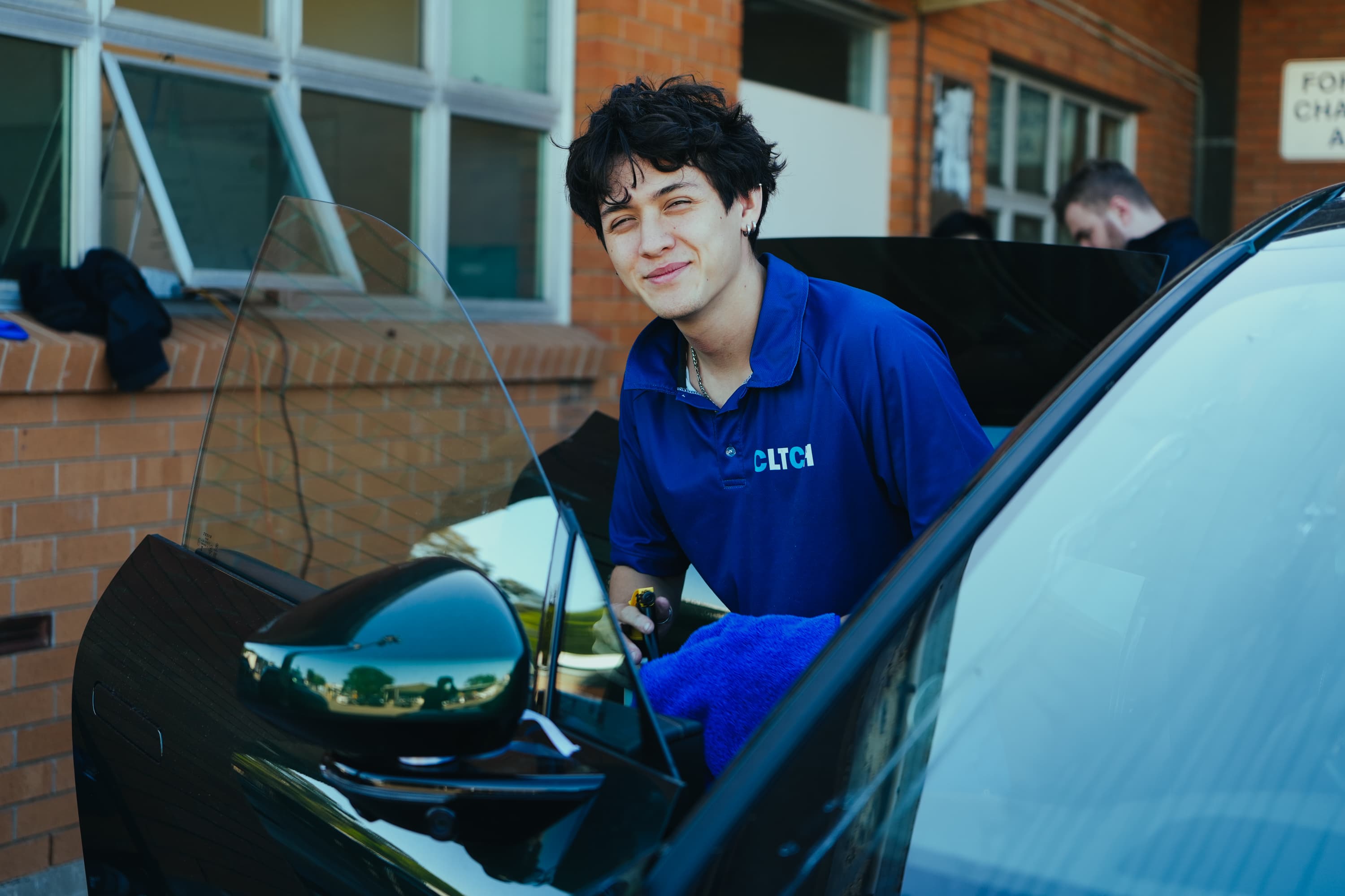 CLTCH detailer working on a car door in the sun